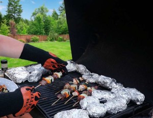 BBQ grill with several potatoes in foil and gloved hand