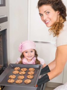 woman and small girl in kitchen taking hot cookies from oven